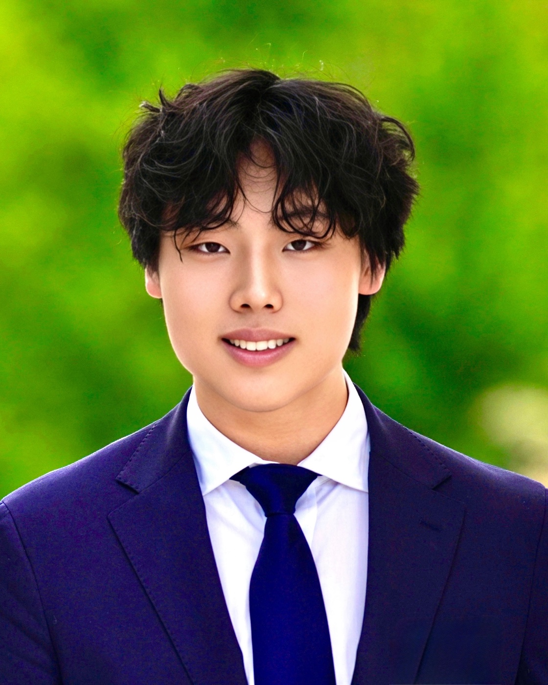 Portrait of David Liu in a navy suit and tie, smiling, photographed outdoors against green foliage.