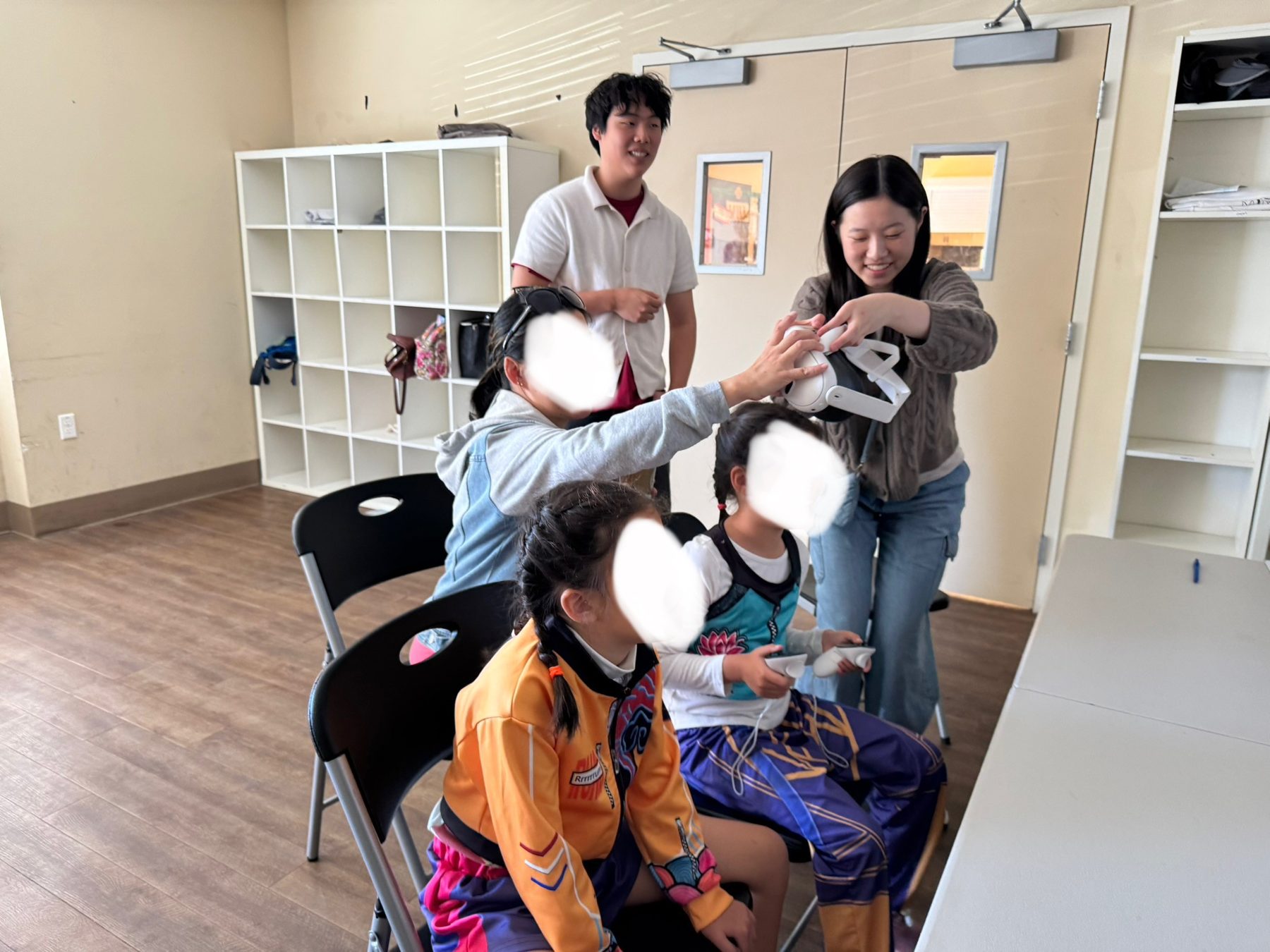 David Liu and a volunteer help two seated children with a small toy at the TWINKLELINK summer camp; the children's faces are obscured.