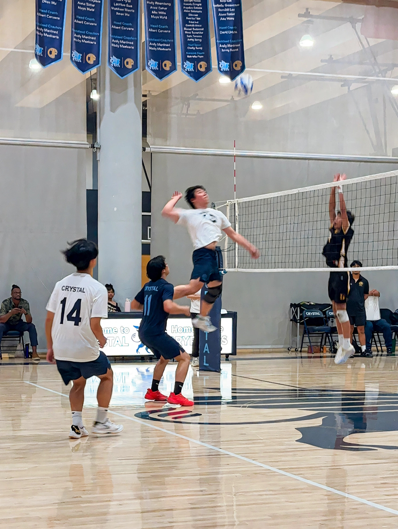 A boys volleyball match in a school gym, a player rising at the net to attack.