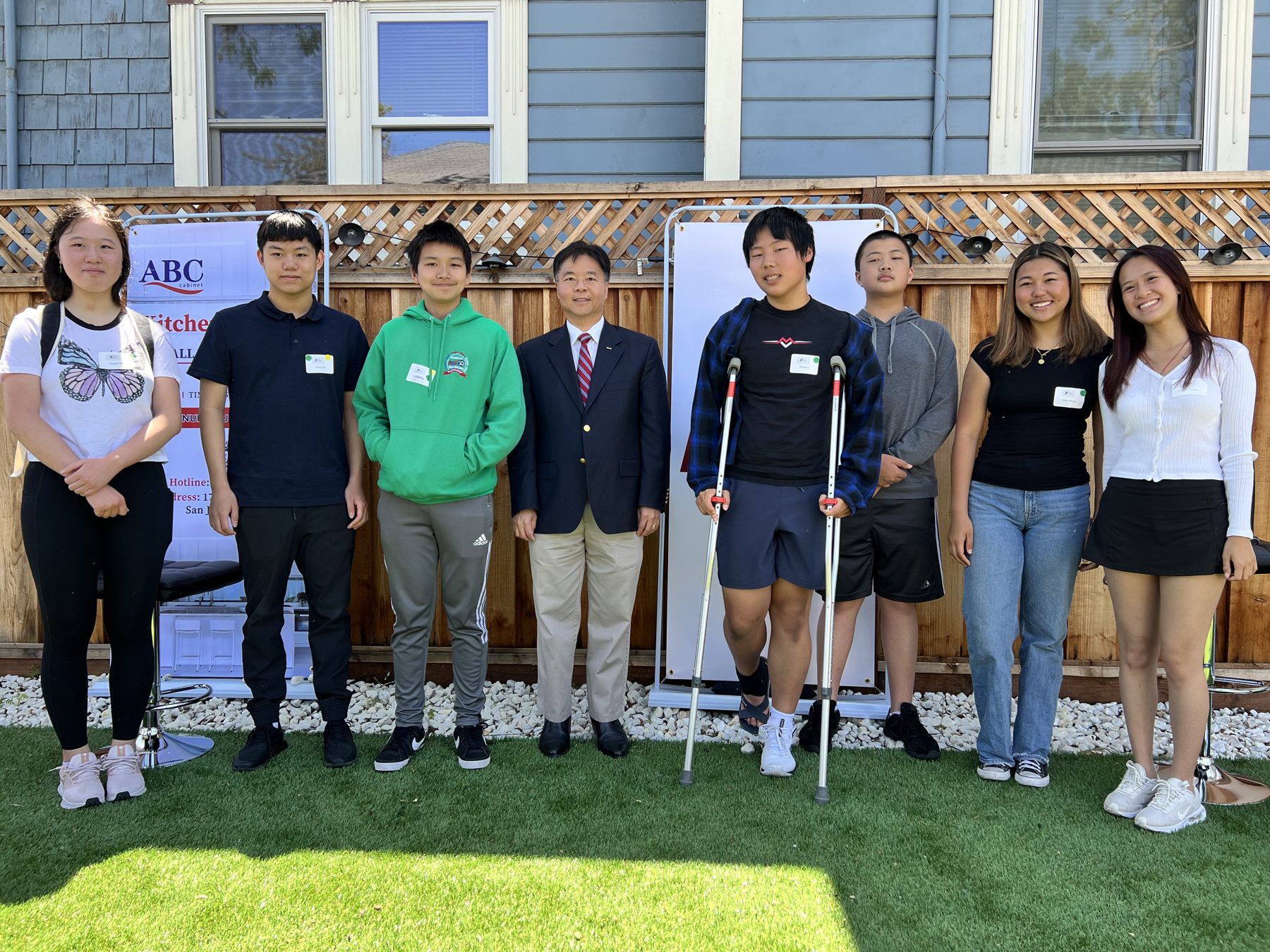 David Liu with fellow members and a guest in a suit, standing on a lawn in front of an event banner.